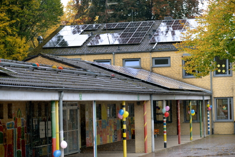 Blick auf die Grundschule Birkstraße in Aachen, ein zweigeschossiges Gebäude aus hellen Backsteinen, grauem Dach und einem eingeschossigen Längsgebäude mit Vordach.