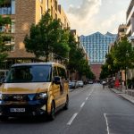 Das Bild zeigt einen ID Buzz AD von Moia auf einer Straße in Hamburg. Im Hintergrund ist die Elbphilharmonie zu erkennen.