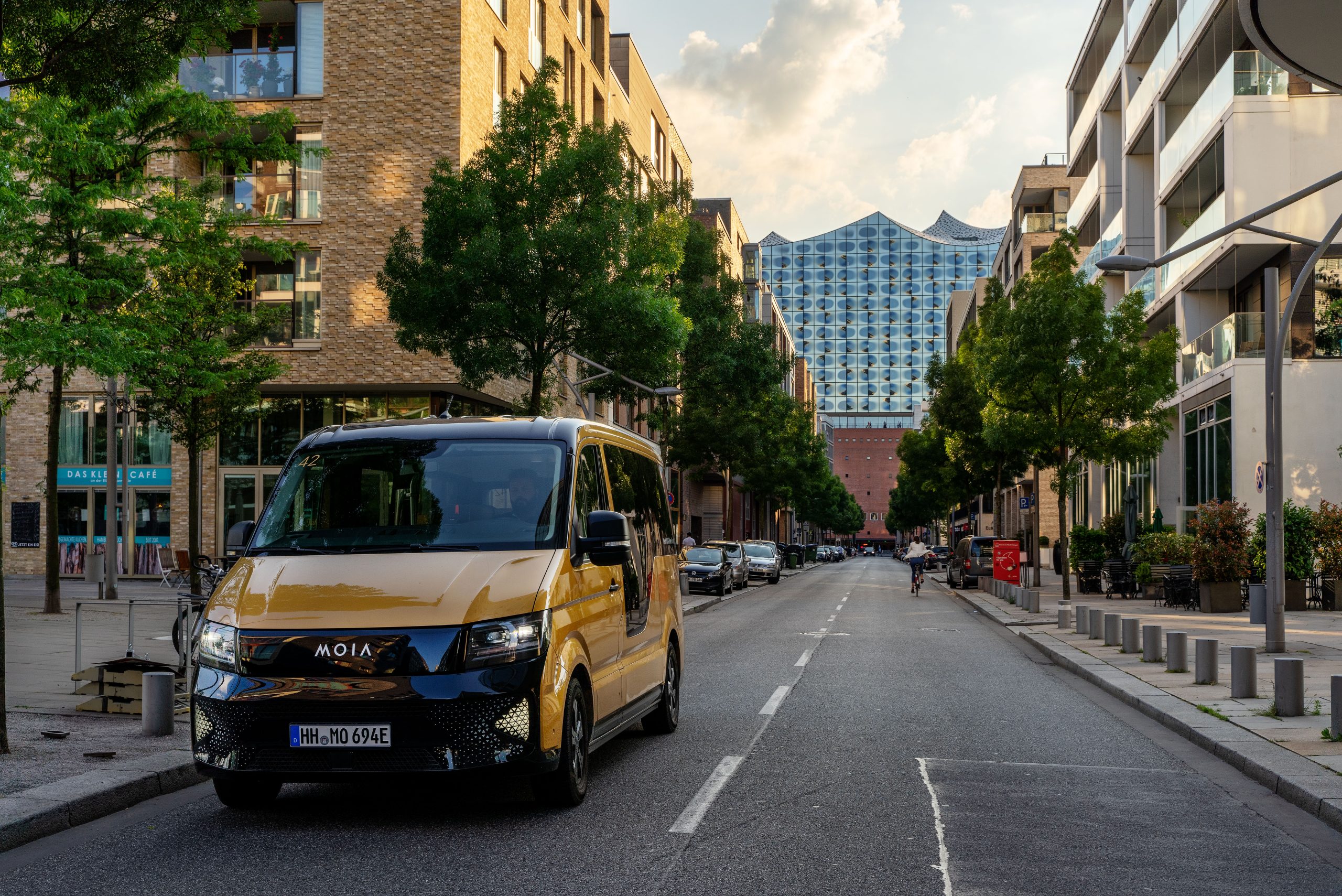 Das Bild zeigt einen ID Buzz AD von Moia auf einer Straße in Hamburg. Im Hintergrund ist die Elbphilharmonie zu erkennen.