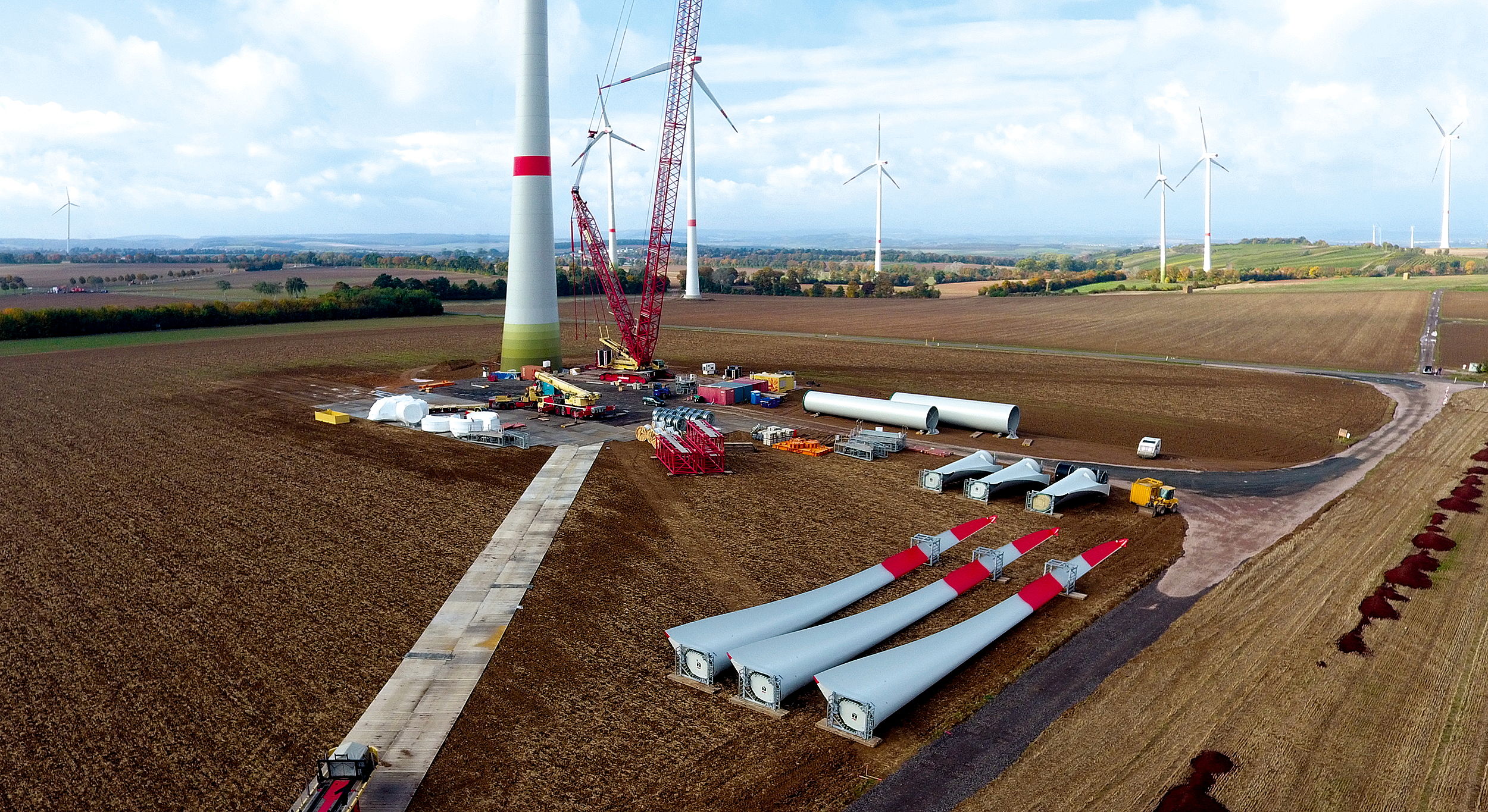 Das Bild zeigt eine Windkraftanlage im Bau. Der Turm steht bereits, im Vordergrund liegen die Rotoren auf dem Boden.