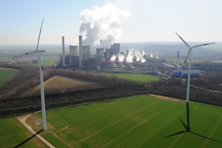 Auf dem Bild ist das Kohlekraftwerk Weisweiler zu sehen, im Vordergrund stehen zwei Windräder.