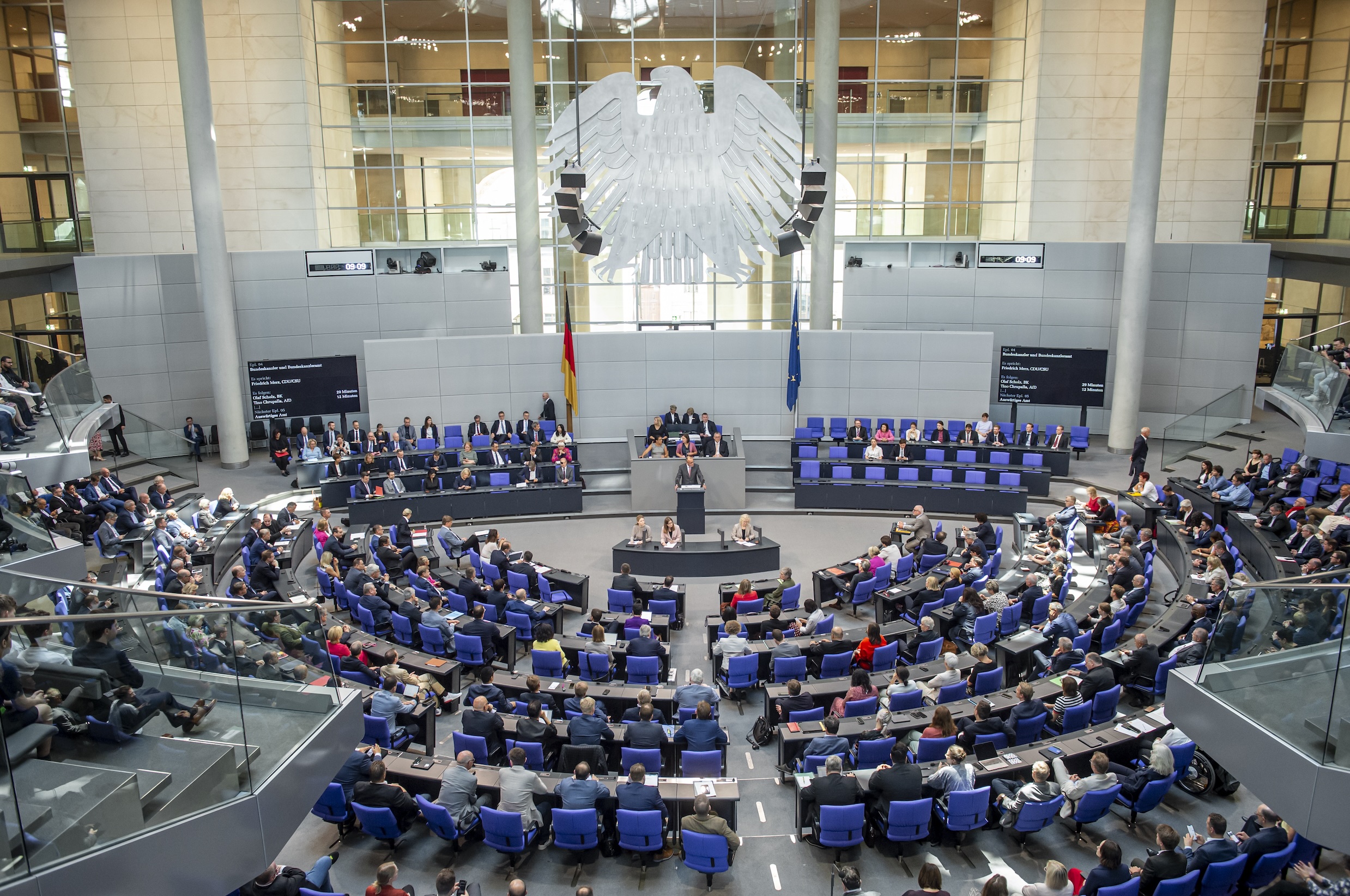 Das Bild zeigt einen Blick in den Plenarsaal des Deutschen Bundestags. Zusehen sind die Reihen der Abgeordneten und im Hintergrund der Bundesadler.